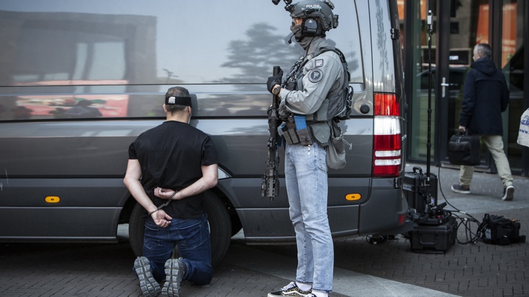 Politieacademie studierichting Aanhouding en interventie - burger zit geknield bij grijze bus onder toezicht van agent in burger