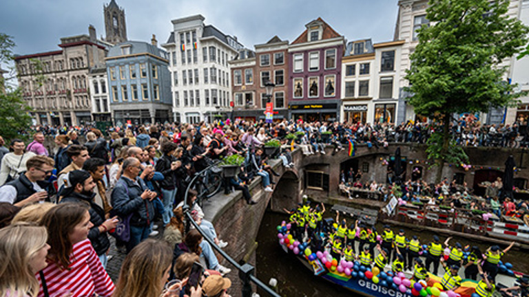 De boot van de politie vaart door de grachten van Utrecht tijdens de Pride, met veel publiek op de kade. 