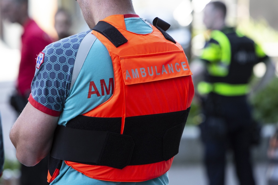 Samenwerkingen Politieacademie - Man met reflecterend oranje vest met tekst Ambulance vanaf de rug gezien