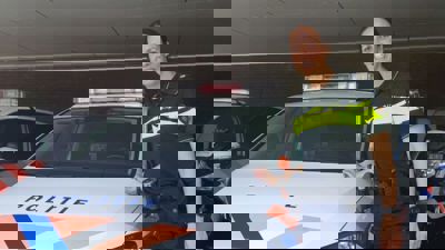 Docent Miranda staat bij een politieauto in een garage