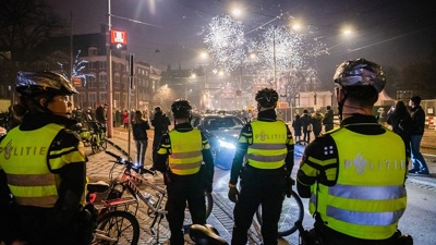 Vier agenten bekijken op een afstand een groep mensen met vuurwerk op de achtergrond tijdens de jaarwisseling