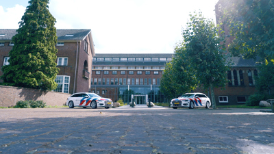 Buitenkant van de Politieacademie Concernlocatie in Apeldoorn met 2 politieauto's