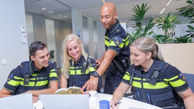 Politiestudenten studeren achter een laptop. Een politiedocent helpt hen.