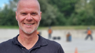 Docent Renko staat in een zwarte polo en lacht naar de camera