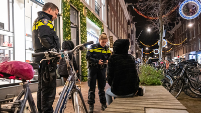 Two police officers approach someone sitting on a bench on the street