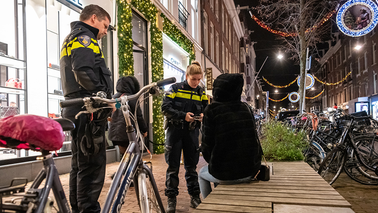 Twee politieagenten spreken iemand aan die op een bankje zit op straat