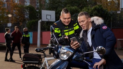 Politieagent in gesprek met jongeman op scooter