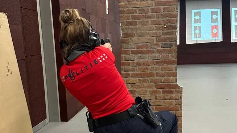 Carmen in rood IBT-shirt achter een wand op de schietbaan