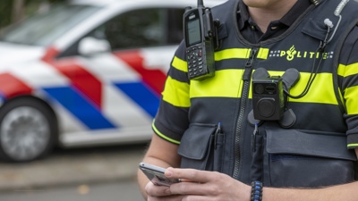 Agent op straat met een mobiele telefoon in de hand, met een politieauto op de achtergrond