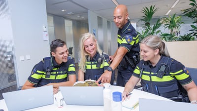 Een docent en drie politiestudenten kijken samen op een laptop en lachen