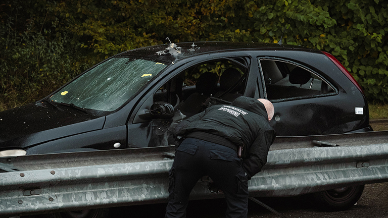 Black exploded car along the crash barrier with someone from the Forensic Investigation