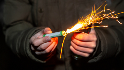 A man holds a firecracker in his hands and lights it; splashes come off the firecracker